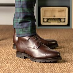 a close up of a person's foot wearing brown shoes and green plaid pants