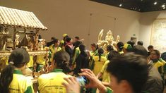 a group of people in yellow and green shirts looking at an art work on display