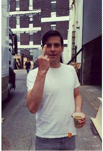 a man is standing on the street and making a peace sign with his hand while holding a drink in one hand