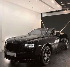 a black rolls royce parked in front of a white wall