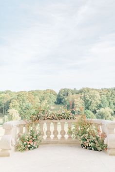 a stone bench with flowers on it in front of trees