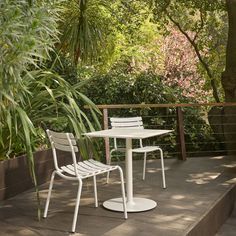 two white chairs and a table on a deck with trees in the backgroud