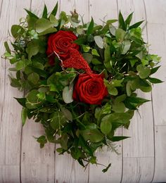 a bouquet of red roses sitting on top of a wooden table next to green leaves