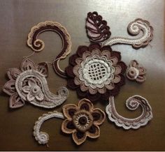 several crocheted flowers and paisleys on a brown tablecloth with white thread