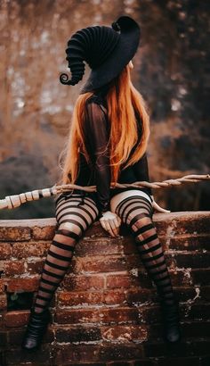 a woman sitting on top of a brick wall wearing black and white striped tights