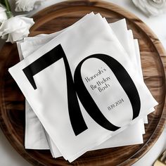 napkins with the number seventy on them are sitting on a wooden plate next to flowers