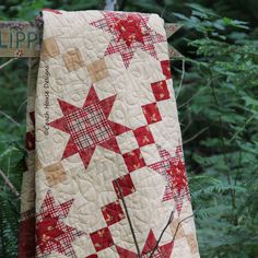 a red and white quilt hanging from the side of a wooden pole with trees in the background