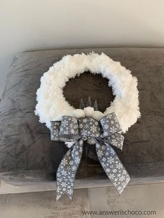 a white wreath sitting on top of a gray pillow next to a black and white bow