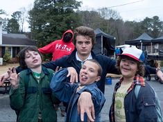 three boys are posing for the camera with their hands in the air and one boy is wearing a red jacket