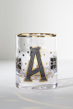 a glass with the letter a on it and some gold dots around it in front of a white background