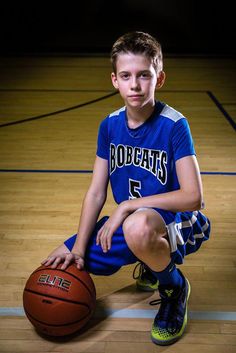 a young boy sitting on the floor with a basketball in his hand and wearing blue