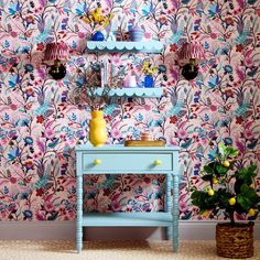 a blue table sitting in front of a pink wallpapered wall with flowers on it