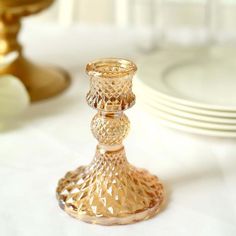 a gold candle holder sitting on top of a table next to white plates and silverware