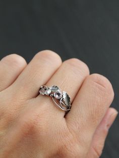 a woman's hand wearing a silver ring with two leaves on the middle and one flower in the middle