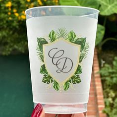 a person holding up a plastic cup with a monogrammed design on the side