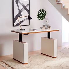 a white table with a plant on it in front of a stair case next to a painting