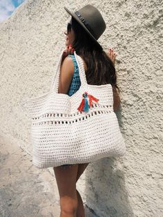 a woman carrying a white crocheted bag on her back, standing in front of a wall