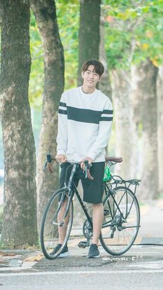 a young man standing next to his bike on the street with trees in the background