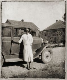 an old black and white photo of a woman standing next to a car