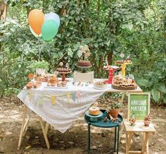 a table topped with lots of desserts and balloons in the air next to trees