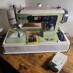 an old green sewing machine sitting on top of a wooden table next to a phone