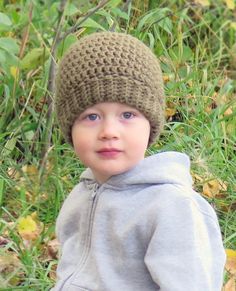 a young boy wearing a knitted hat in the grass with leaves around him and looking at the camera