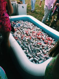 an inflatable pool filled with lots of soda cans on the ground and people standing around