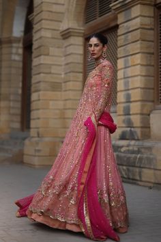 a woman in a pink and gold lehenga standing on the street with her arms behind her back