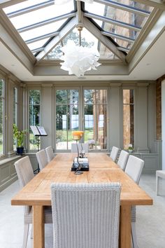 a large wooden table surrounded by chairs in a room with glass walls and skylights