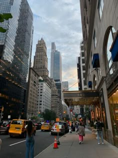 people are walking on the sidewalk in front of tall buildings and skyscrapers at dusk