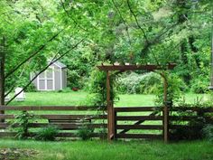 a wooden gate in the middle of a lush green field next to a shed and trees