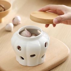 a person is holding a wooden spoon over a small white vase with garlic in it