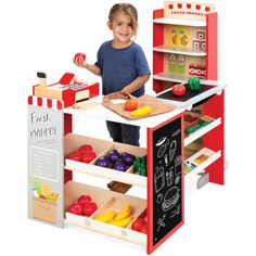 a young boy standing in front of a toy kitchen with fruits and vegetables on it