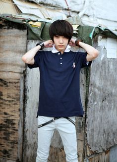 a young man standing in front of a wooden building with his hands on his head