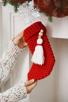 a woman is holding up a red knitted christmas stocking