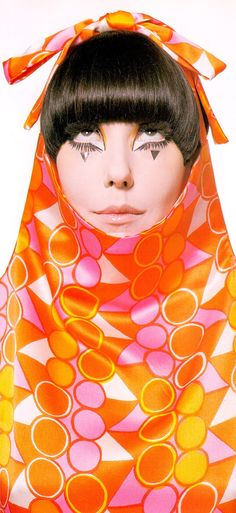 a woman with black hair wearing an orange and pink scarf over her head, in front of a white background