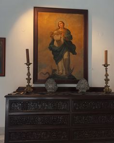 a painting is hanging on the wall above a dresser with candles and vases in front of it