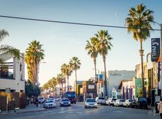 cars are driving down the street in front of shops and palm trees on a sunny day