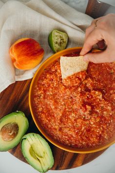 someone dipping some tortilla chips into a bowl of chili and avocado