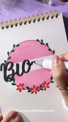 a woman is painting the word blo on a piece of paper with flowers and leaves