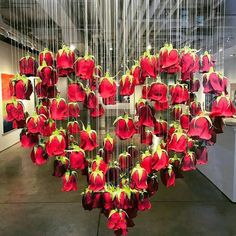 a heart shaped sculpture with red flowers hanging from it's sides in an art gallery