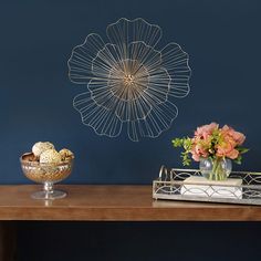 two vases on a table with flowers and an object hanging from the wall behind them