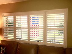 a living room filled with furniture and windows covered in white shutters, next to a lamp