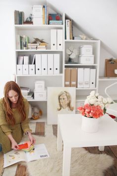 a woman sitting on the floor in front of a bookshelf reading a book