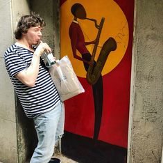 a man standing in front of a painting holding a bag and drinking from a water bottle