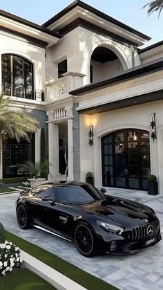 a black sports car is parked in front of a large house with palm trees and shrubs