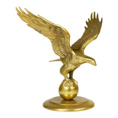 a golden eagle figurine sitting on top of a gold ball with its wings spread