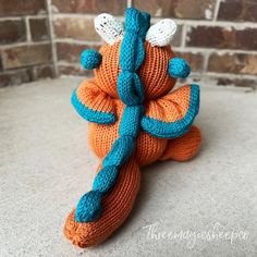 an orange and blue knitted toy sitting on top of a white floor next to a brick wall