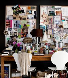 two white chairs sitting in front of a desk covered with papers and pictures on the wall