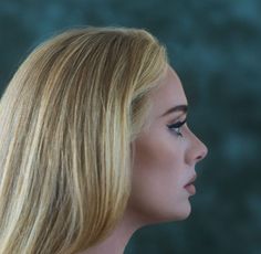 a woman with long blonde hair and blue eyes looks off into the distance while standing in front of a dark background